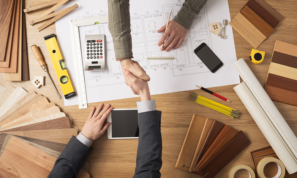 Architect and customer businessman shaking hands top view, desktop with building project, tools and wood swatches on background